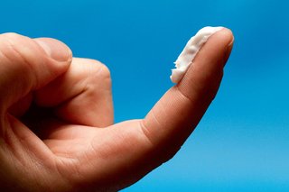 An adult's right hand with their index finger extended. There is a strip of white cream from the tip down to the first crease of their finger.