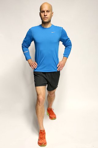 A man standing with his right leg, slightly bent, in front of him. His left leg is stretched out straight behind him, with the heel flat on the floor