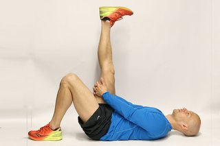 A man lying on his back holding his right leg towards the ceiling