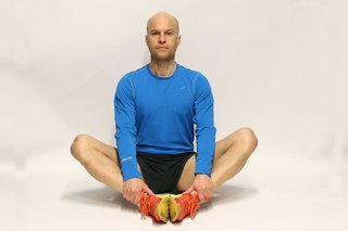 A man sitting on the floor with the soles of his feet together and his hands resting on his ankles